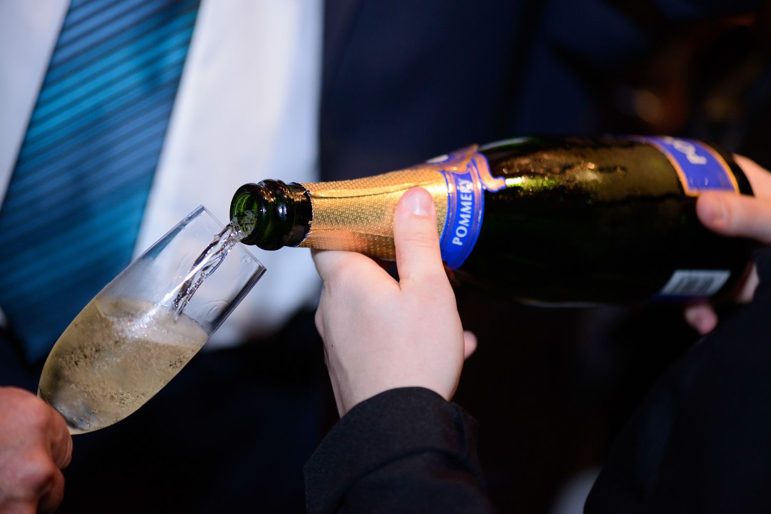 Close-up of hands pouring wine into glasses at formal event.