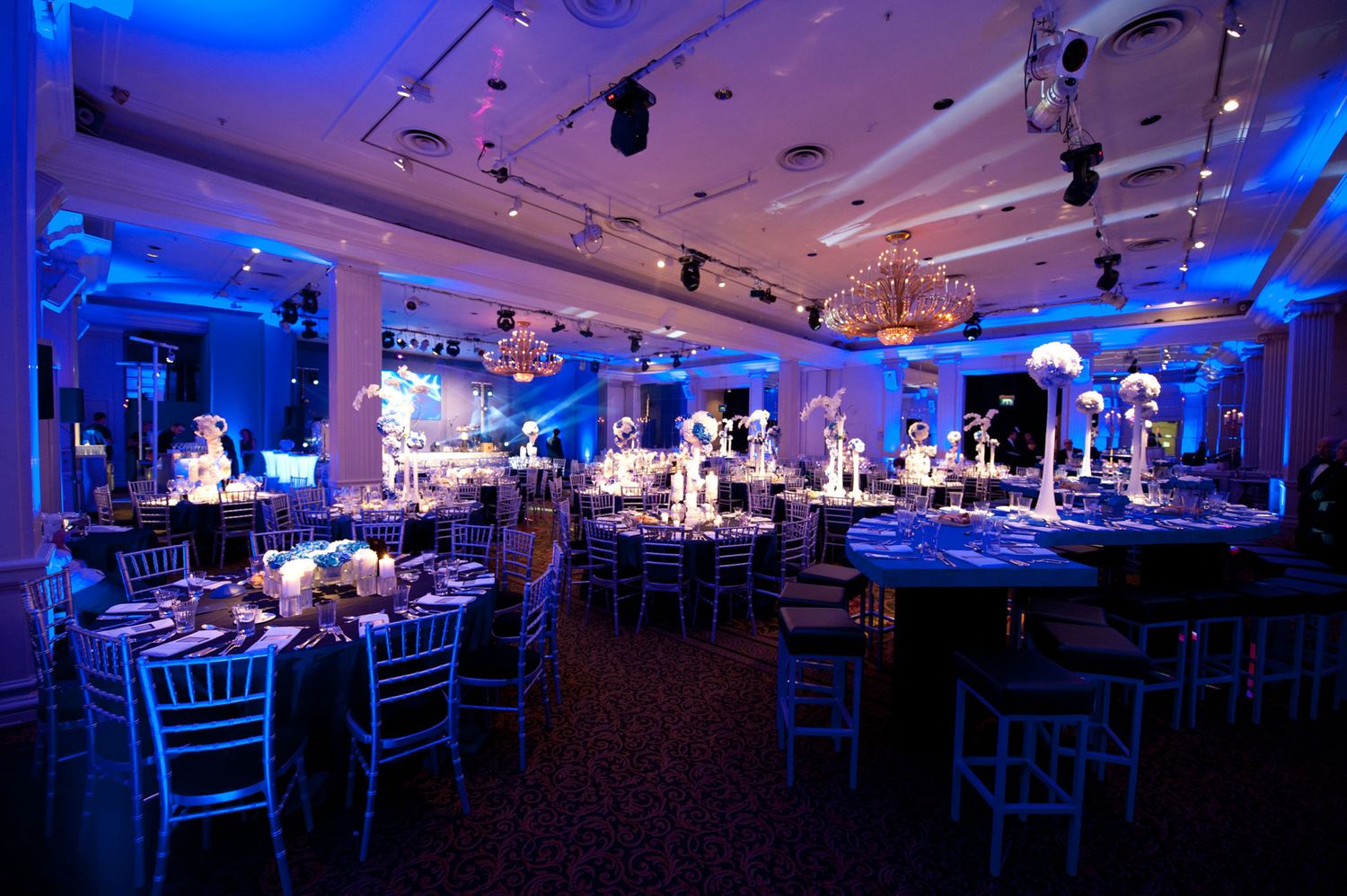 Large banquet hall with blue uplighting and white chairs set up for an elegant evening event.