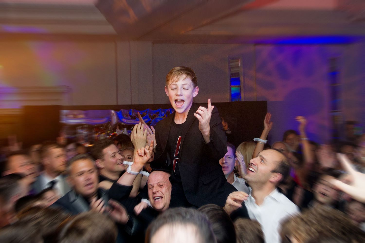 Concert crowd reacts enthusiastically with raised arms and excited expressions during a live music performance.