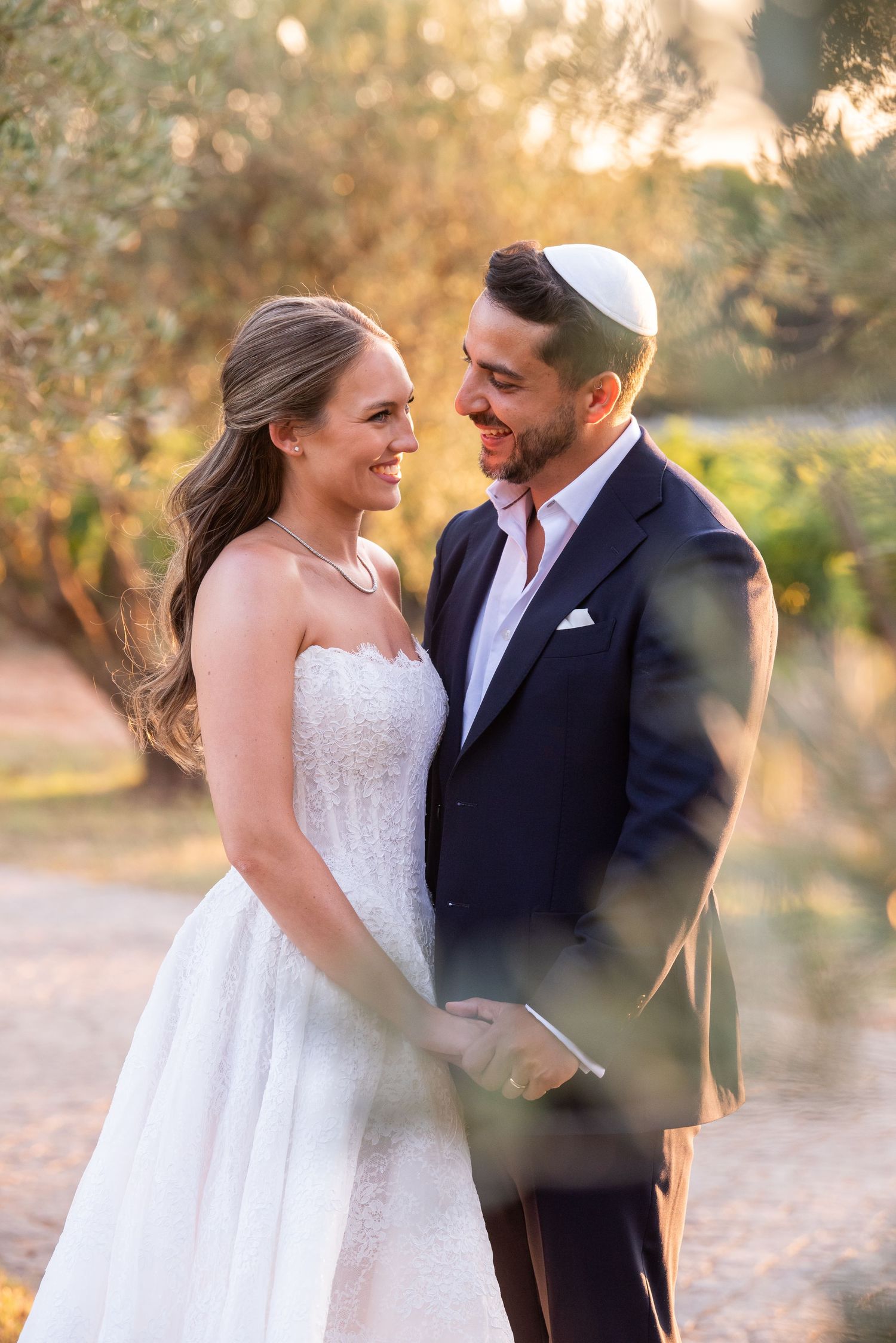 A couple in wedding attire shares intimate moments during a golden hour photoshoot in an outdoor setting.