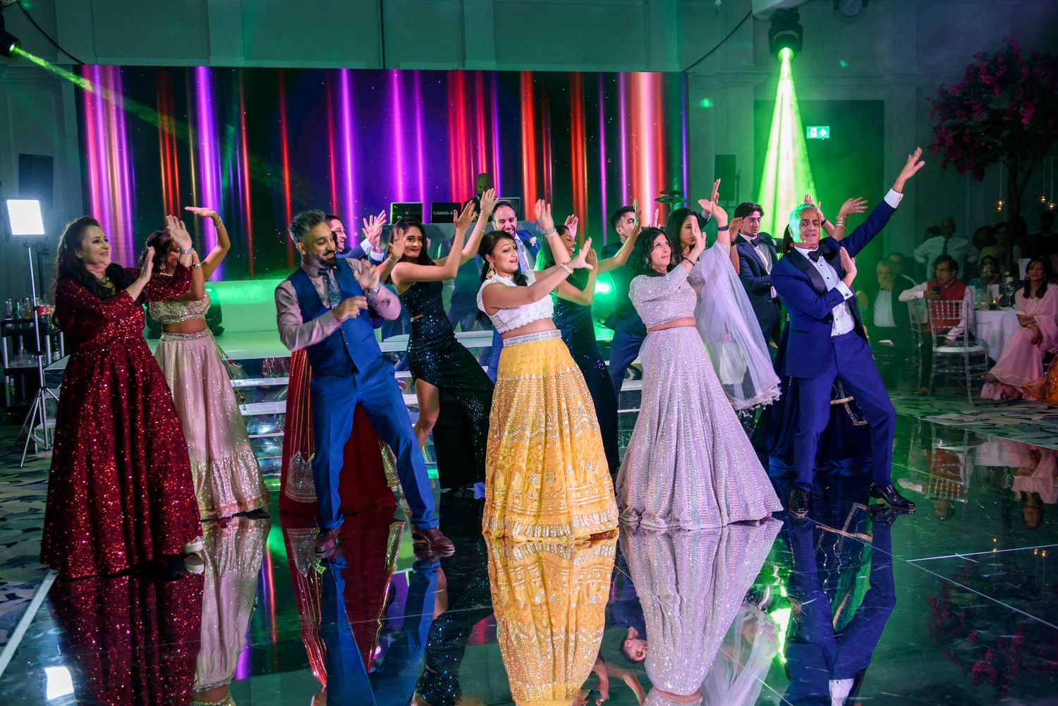 Group of guests dancing in colorful traditional Indian attire at a vibrant wedding reception celebration.