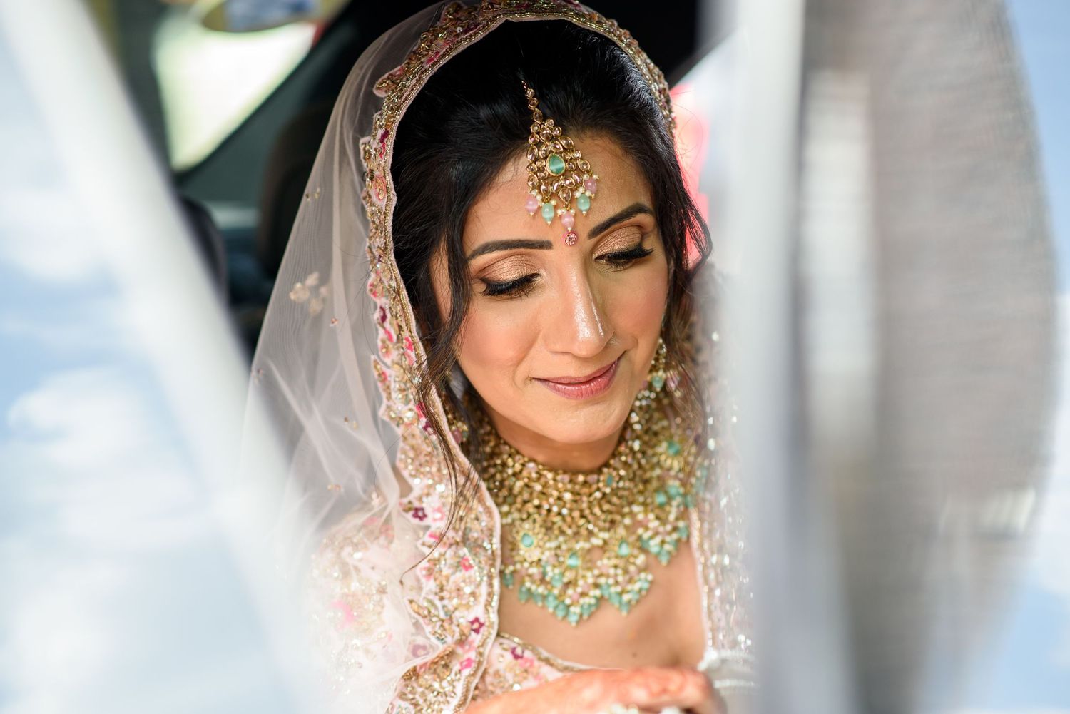 South Asian bride in traditional gold and green jewelry with embroidered dupatta looking down gracefully.
