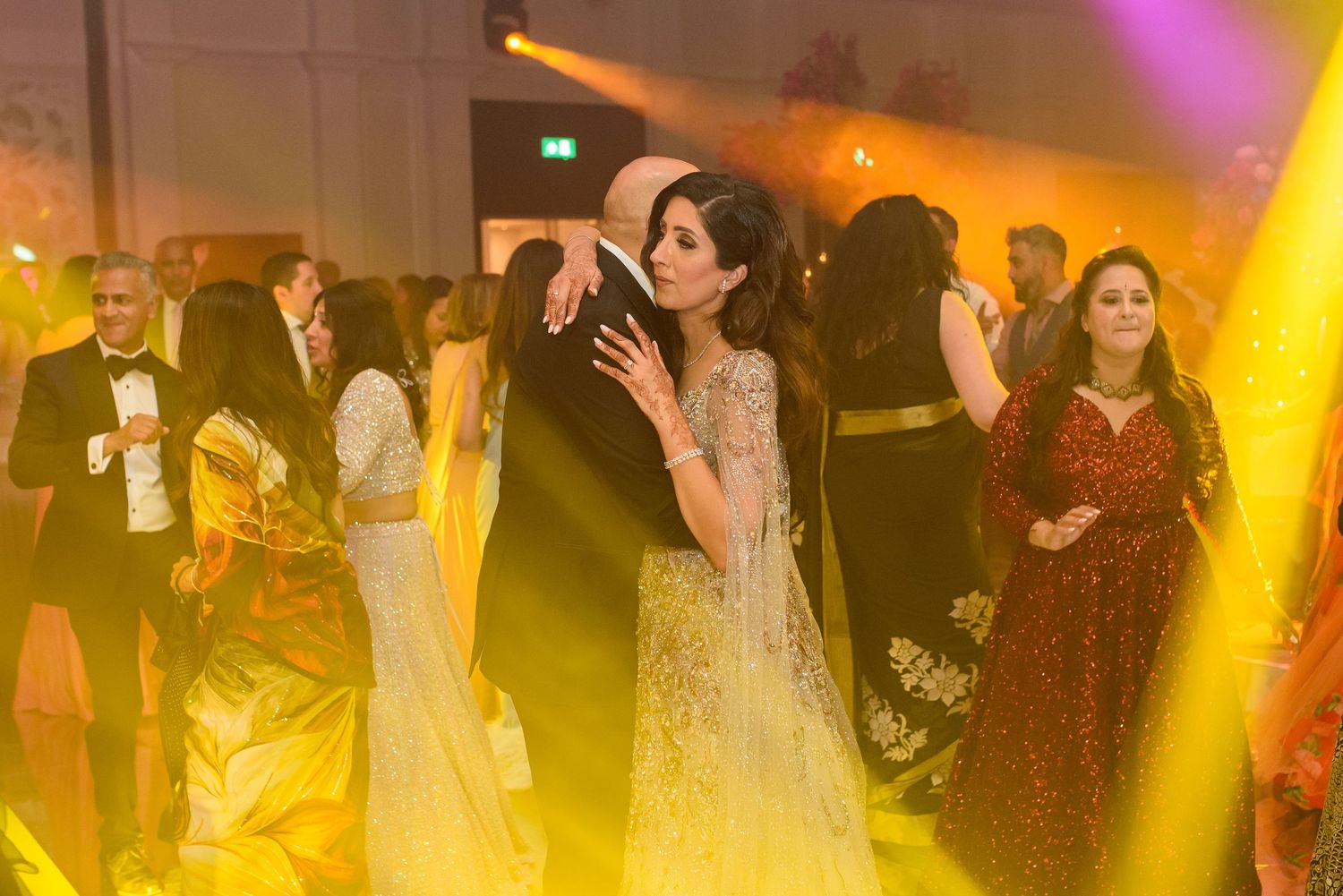 Guests dancing at an elegant evening celebration with warm yellow lighting and formal attire.