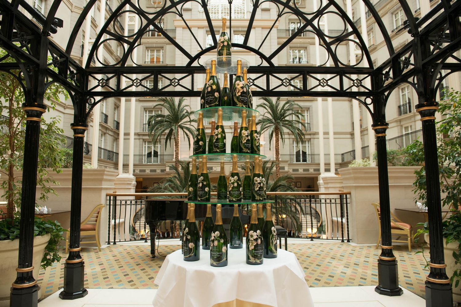 Ornate glass ceiling architecture with decorative black metalwork and hanging plants in an atrium.