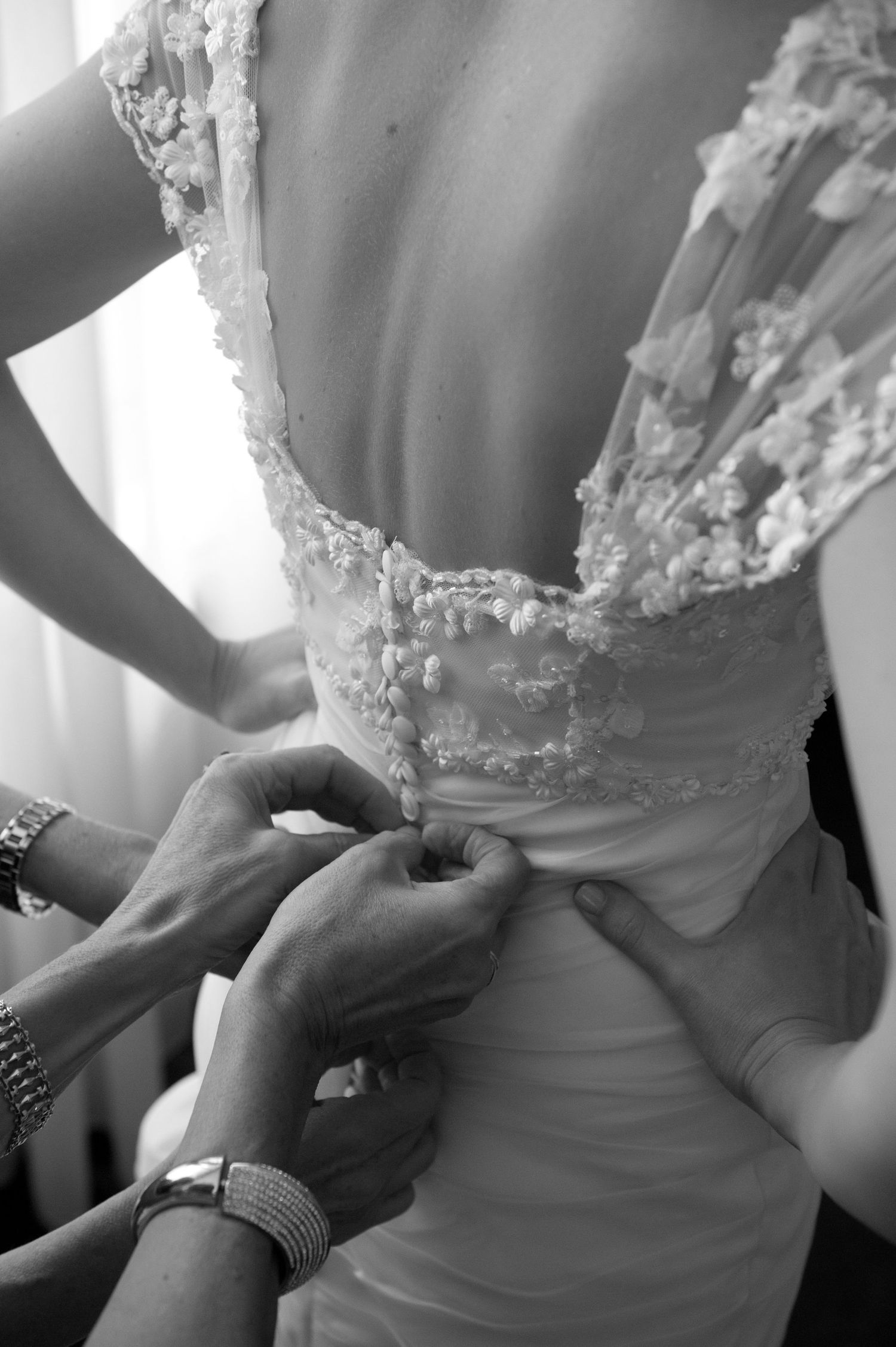 Close-up sequence of hands adjusting and fastening a white wedding dress corset back.