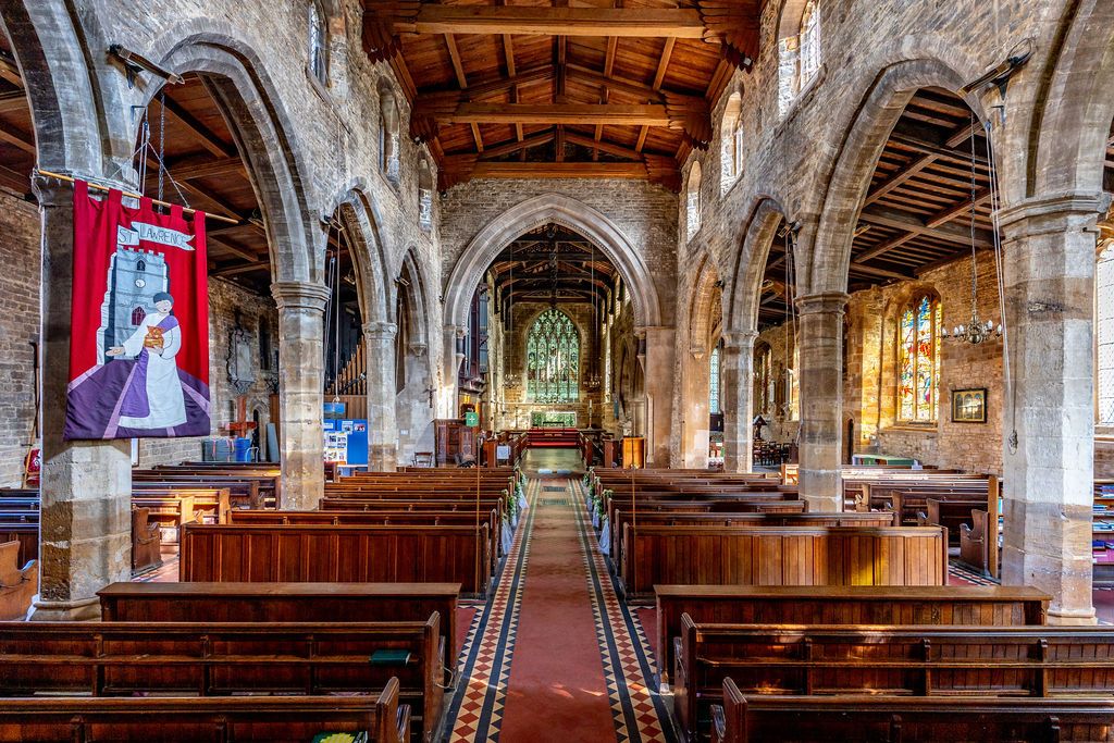Interior of a historic stone church with wooden pews, arched ceilings, stained glass windows, and a colorful banner on display.