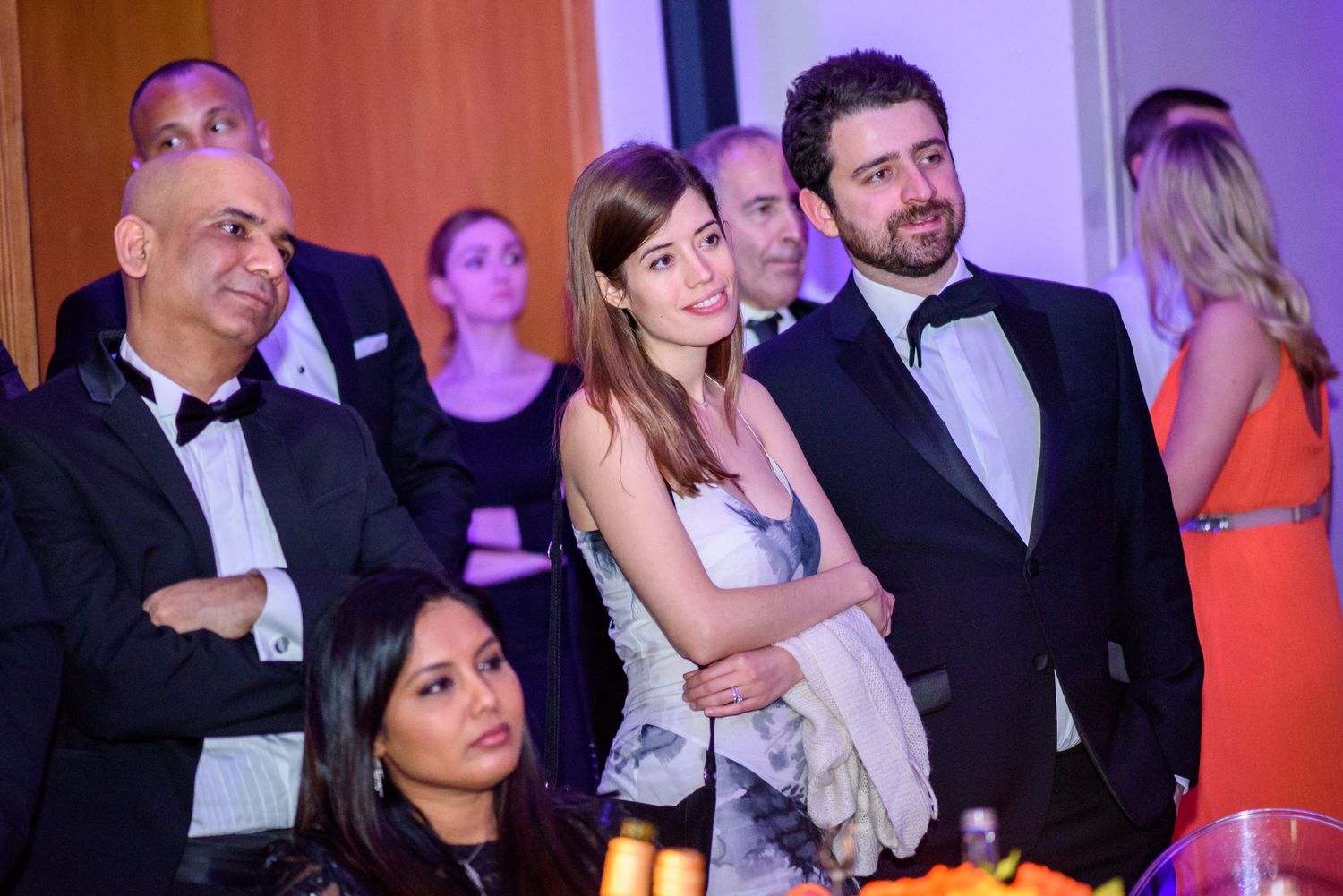 Formal gala event with guests in evening attire under colorful lighting.