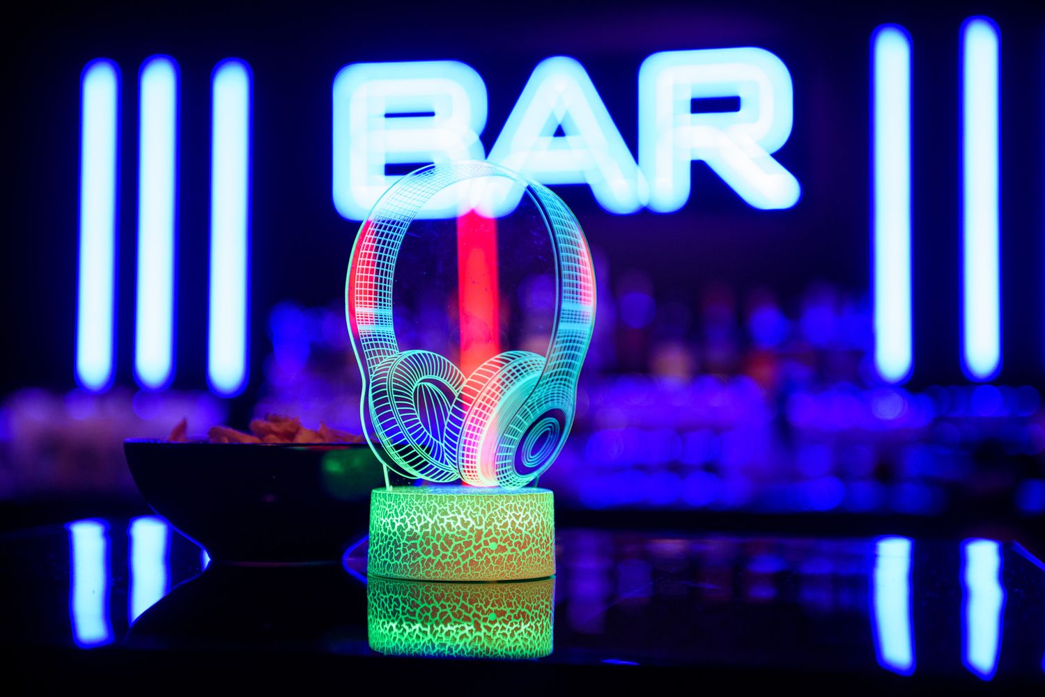 Illuminated neon bar signs and lights create a vibrant nightlife atmosphere with blue and purple hues.