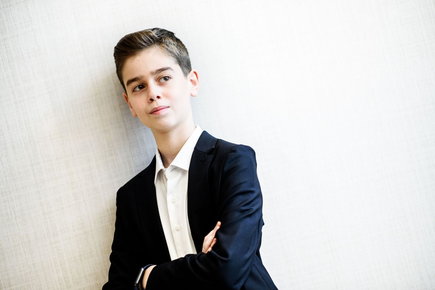 A person in a navy blue suit jacket and white shirt poses against a light colored wall.