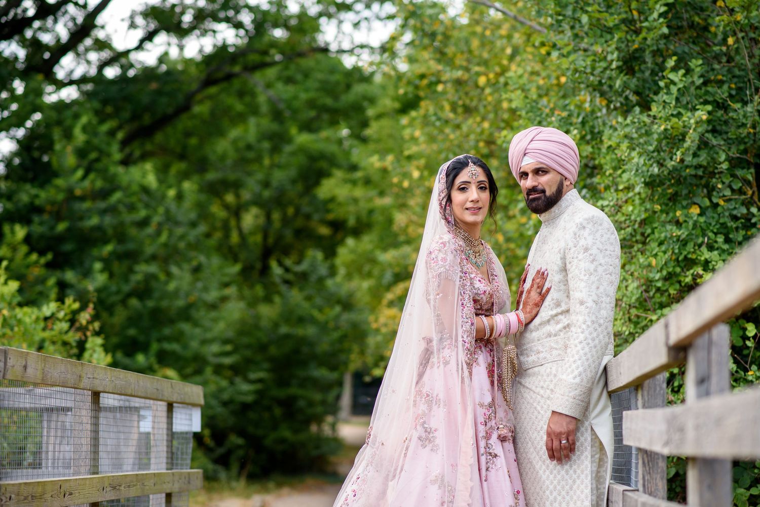A couple in traditional Indian wedding attire pose together in a lush garden setting.