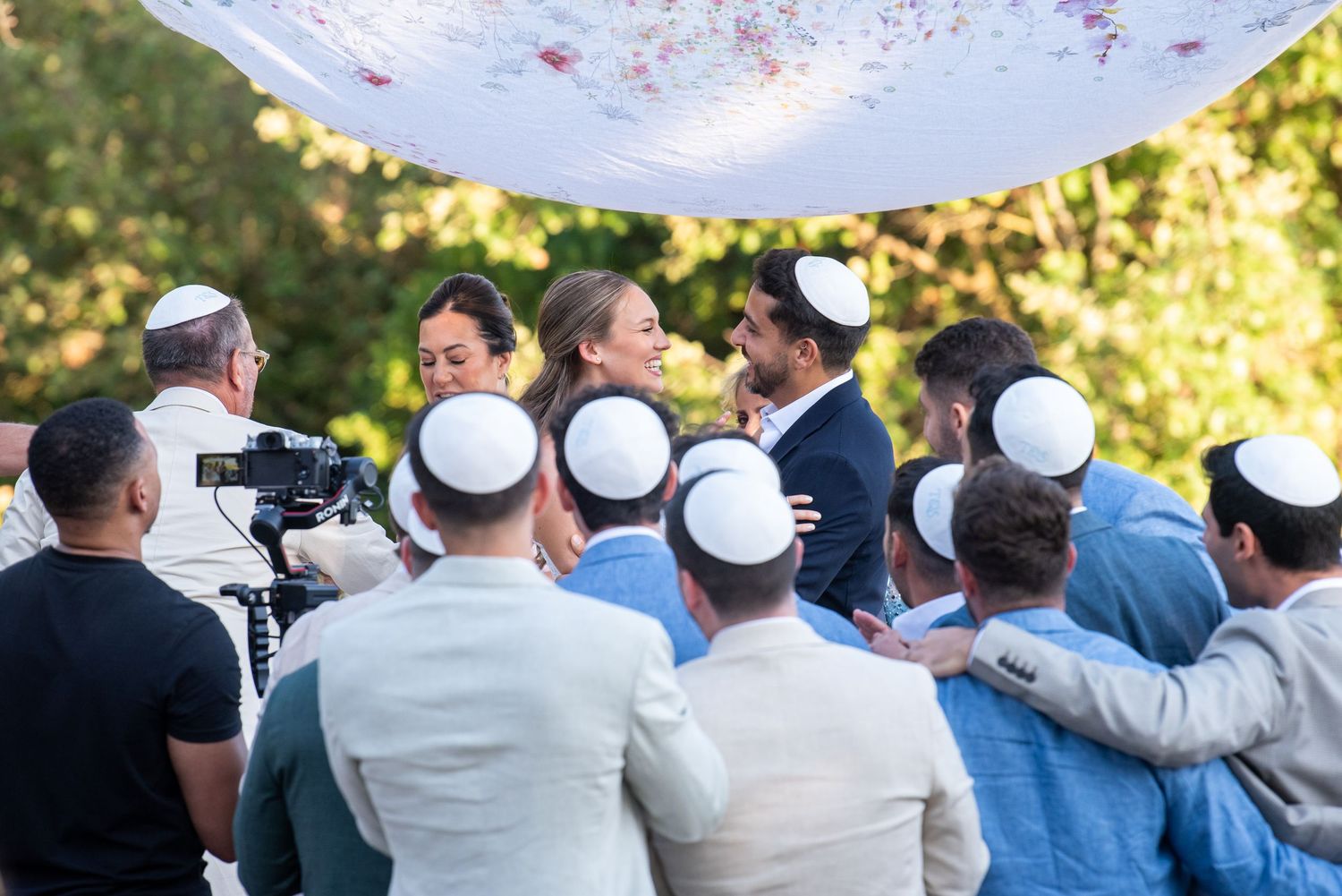 A group of people wearing white kippah head coverings gather outdoors during a celebration.