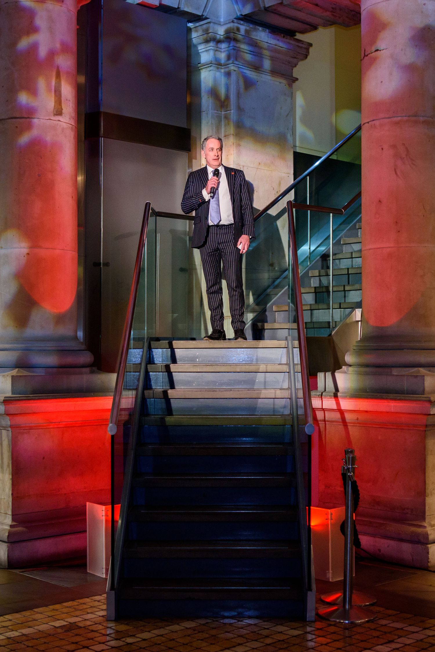 Architectural staircase with dramatic red lighting and columns in an elegant venue setting.