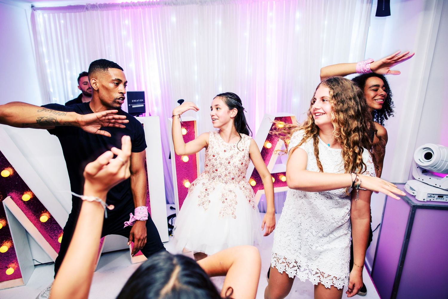 People dancing and celebrating at a lively party with pink and purple lighting in the background.