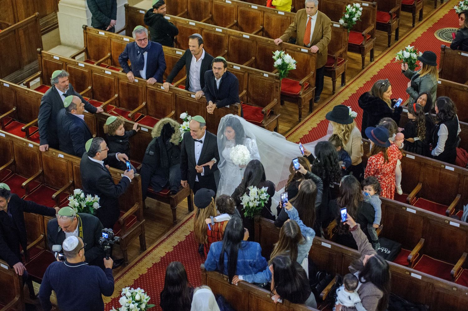 Overhead view of a wedding ceremony in a church with wooden pews decorated with white floral arrangements.