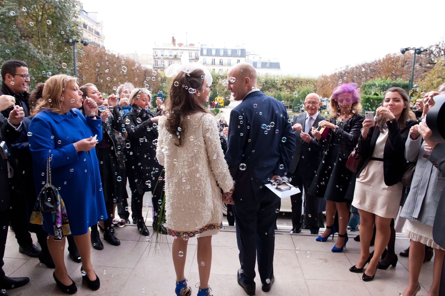 Wedding guests throw confetti and celebrate outside during a festive outdoor ceremony.