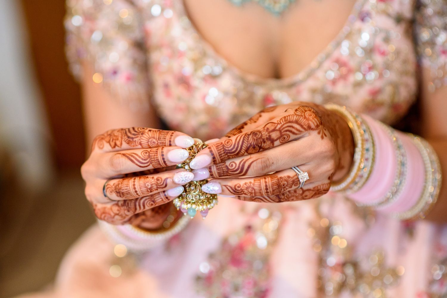 Close-up of bride's hands adorned with intricate henna mehndi designs, bangles, and rings in traditional Indian bridal attire.