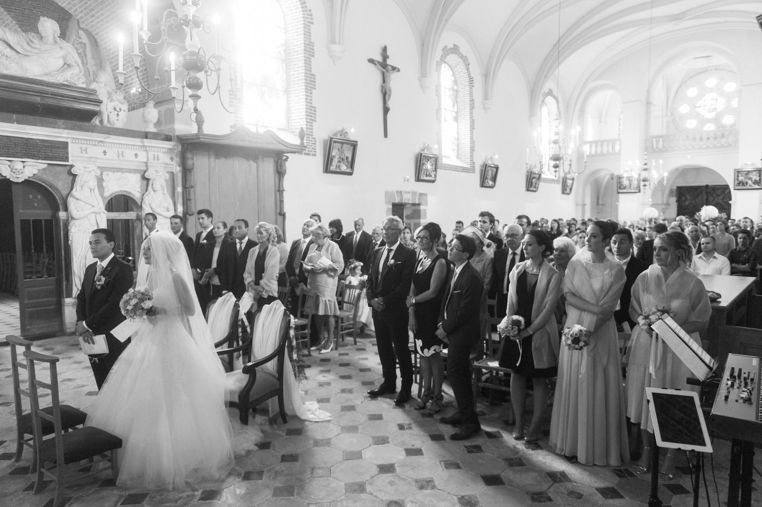 Black and white photo of a wedding ceremony inside a historic church with guests standing in the aisle.