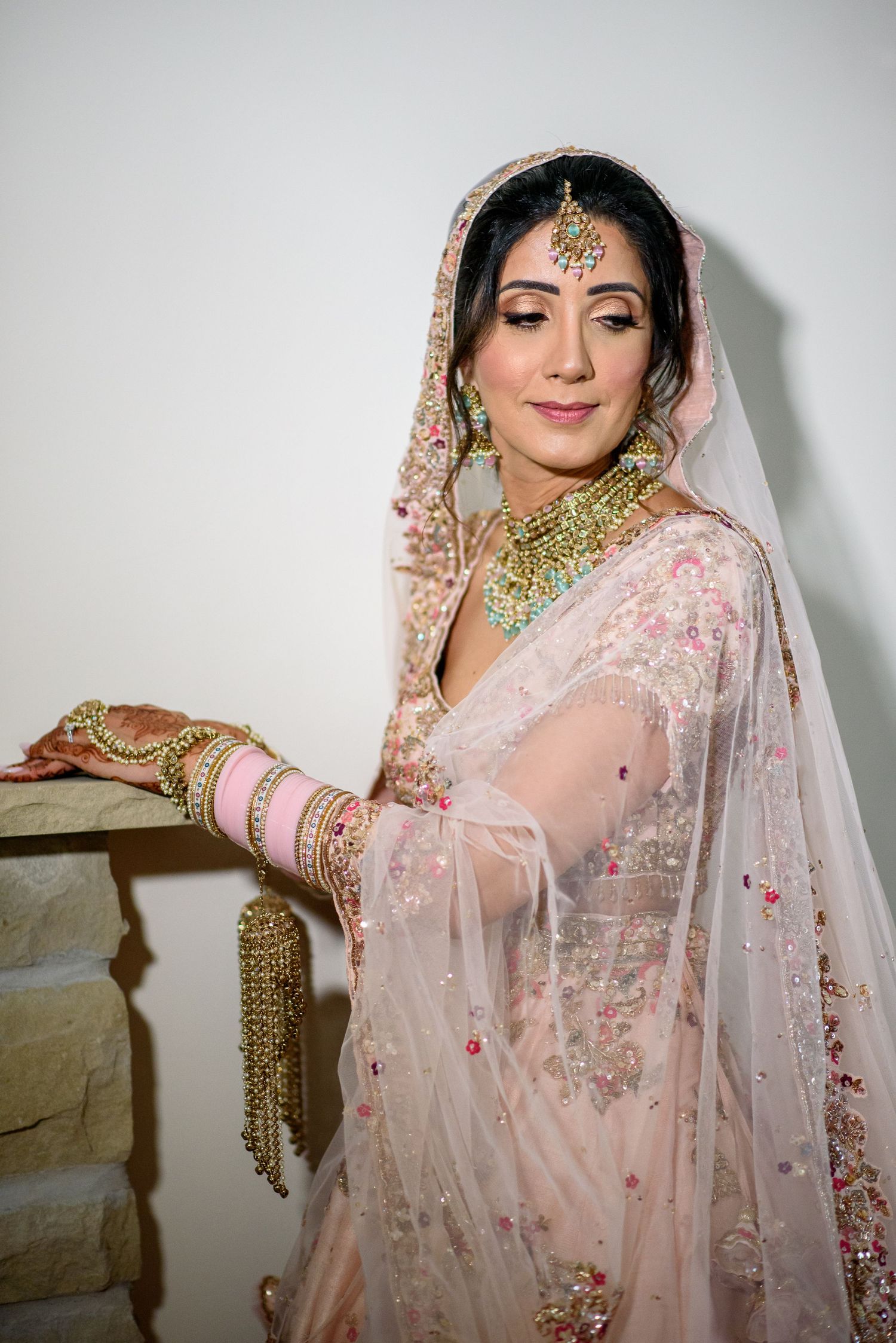 Beautiful traditional South Asian bridal attire featuring pink embroidered lehenga with ornate gold jewelry and veil.