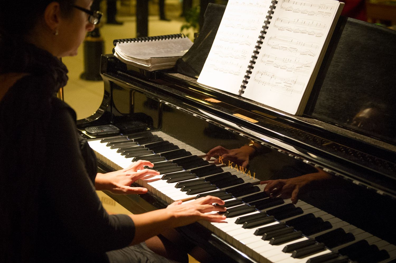 Pianist performing at a grand piano with sheet music illuminated.
