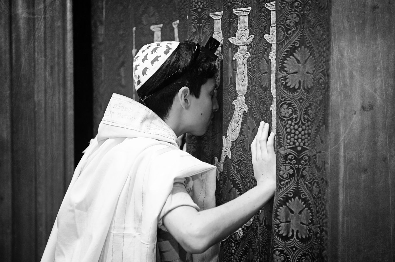Person wearing tefillin and tallit prays at a synagogue wall.