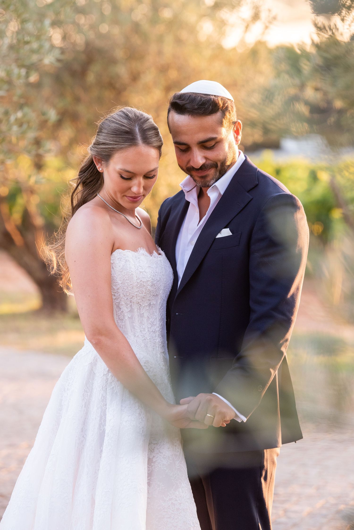 Bride and groom share an intimate moment outdoors at golden hour, groom wearing a kippah and navy suit.
