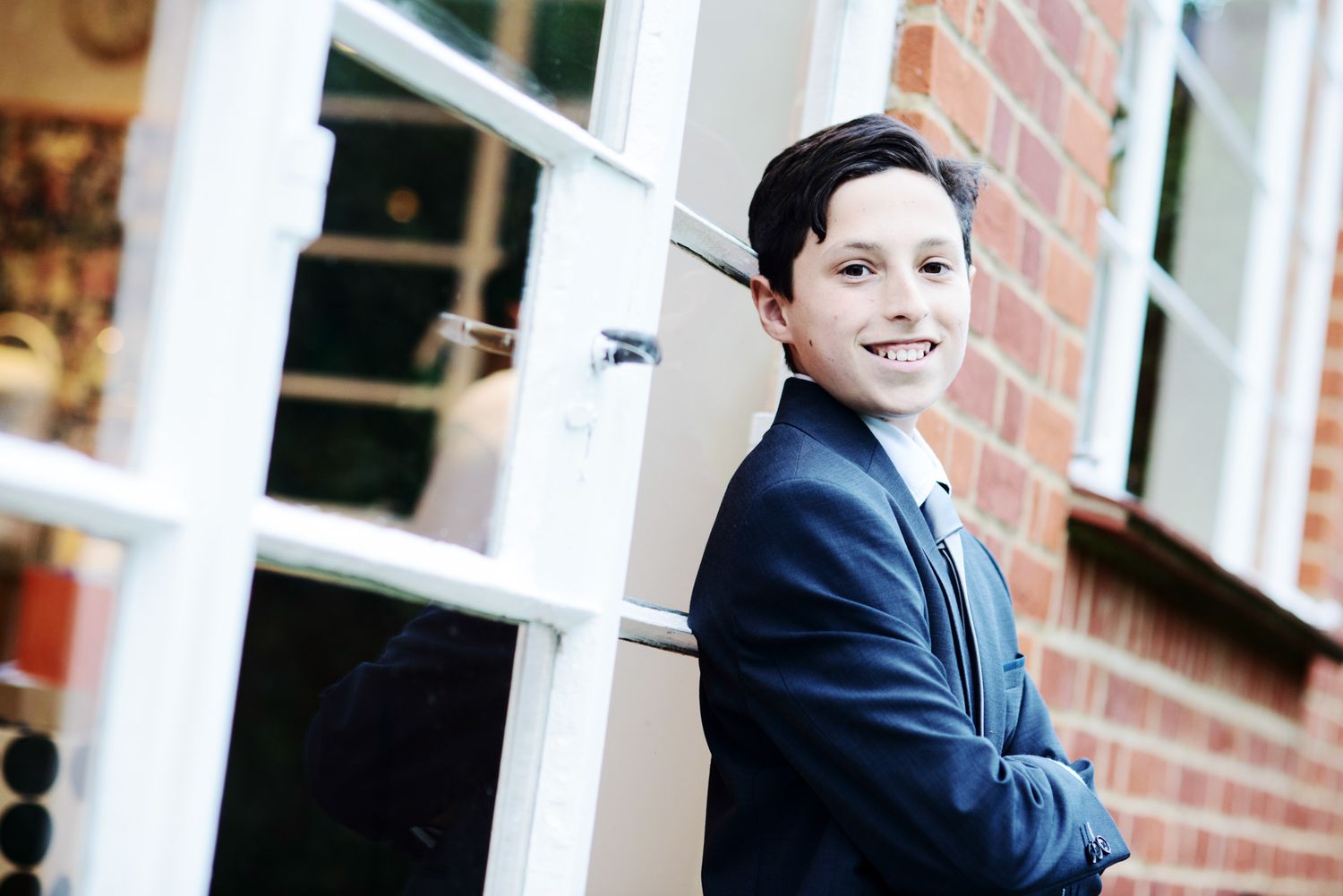 A young student in a navy blue blazer poses for school photos against a brick wall backdrop.