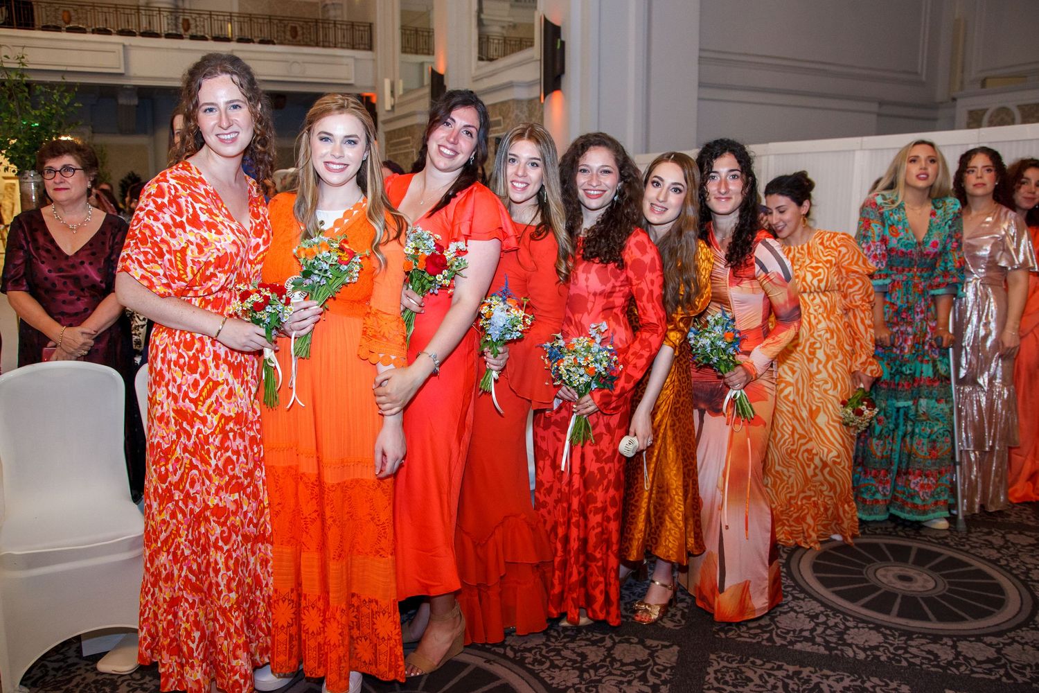 Group of people wearing coordinated orange and red floral dresses gather for a celebratory event.
