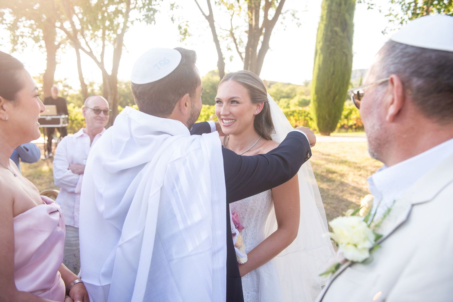 Wedding guests gather outdoors in a sunny garden setting during a joyful celebration.