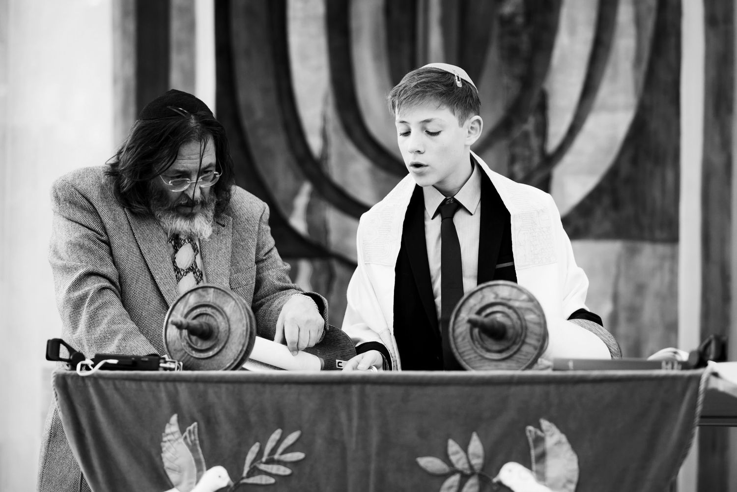Two people stand at a podium with a decorative banner, performing a ceremony in black and white.