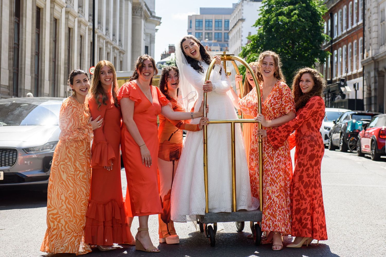 A group wearing coordinated coral and orange floral dresses poses together on a city street.