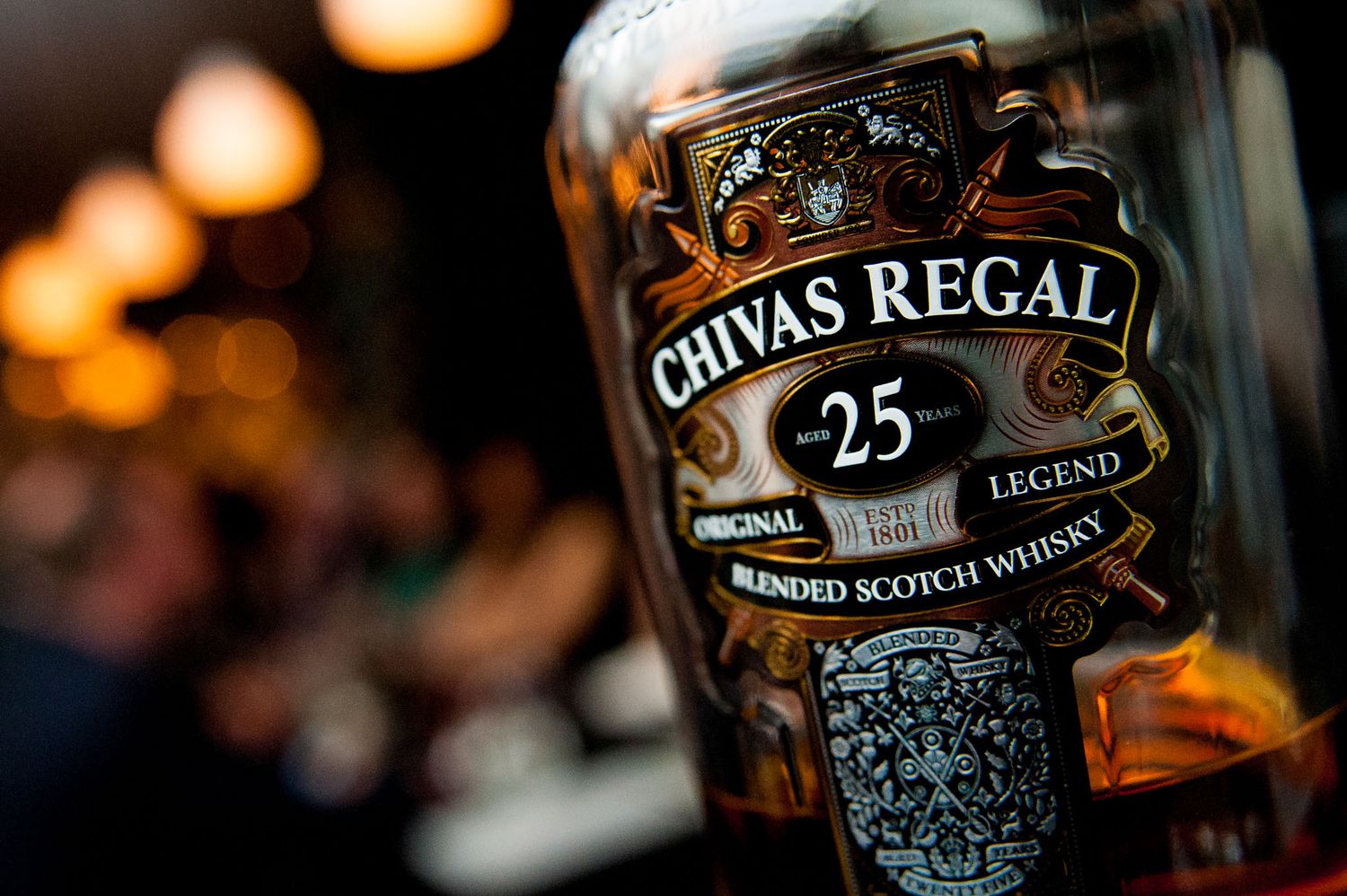 Chivas Regal whisky bottles displayed with warm ambient lighting.
