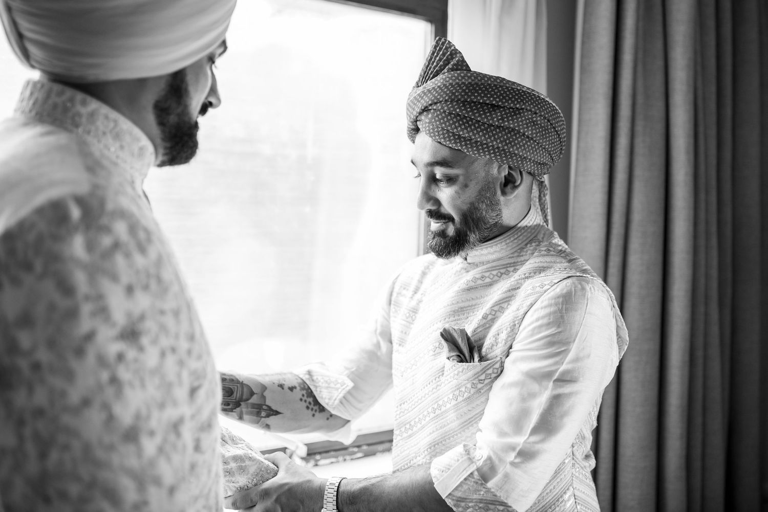 A black and white photograph shows two men in traditional Sikh turbans and formal attire having a conversation.