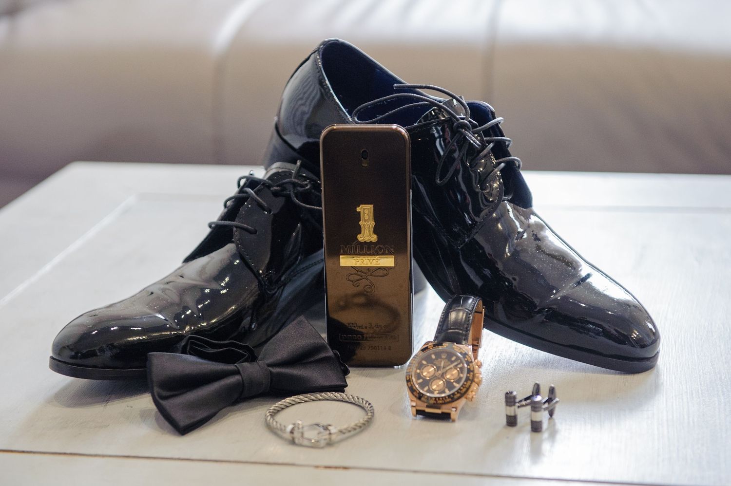 A series of black leather dress shoes arranged with accessories and a watch on a light colored surface.