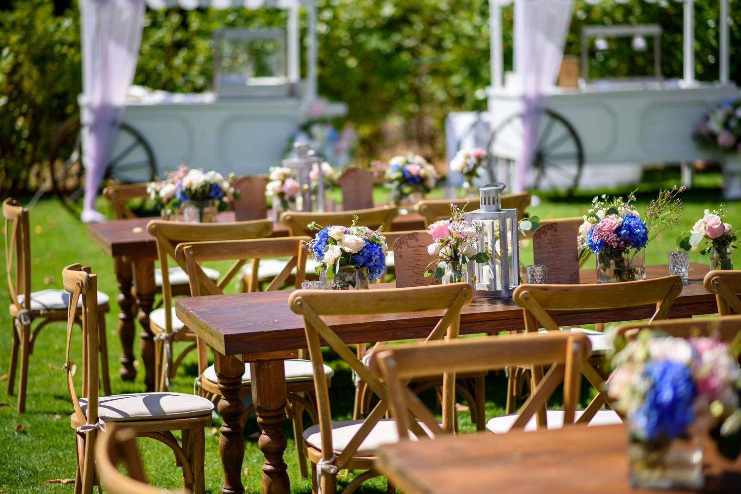 Rustic wooden chairs with blue floral decorations arranged outdoors for an elegant garden wedding ceremony.