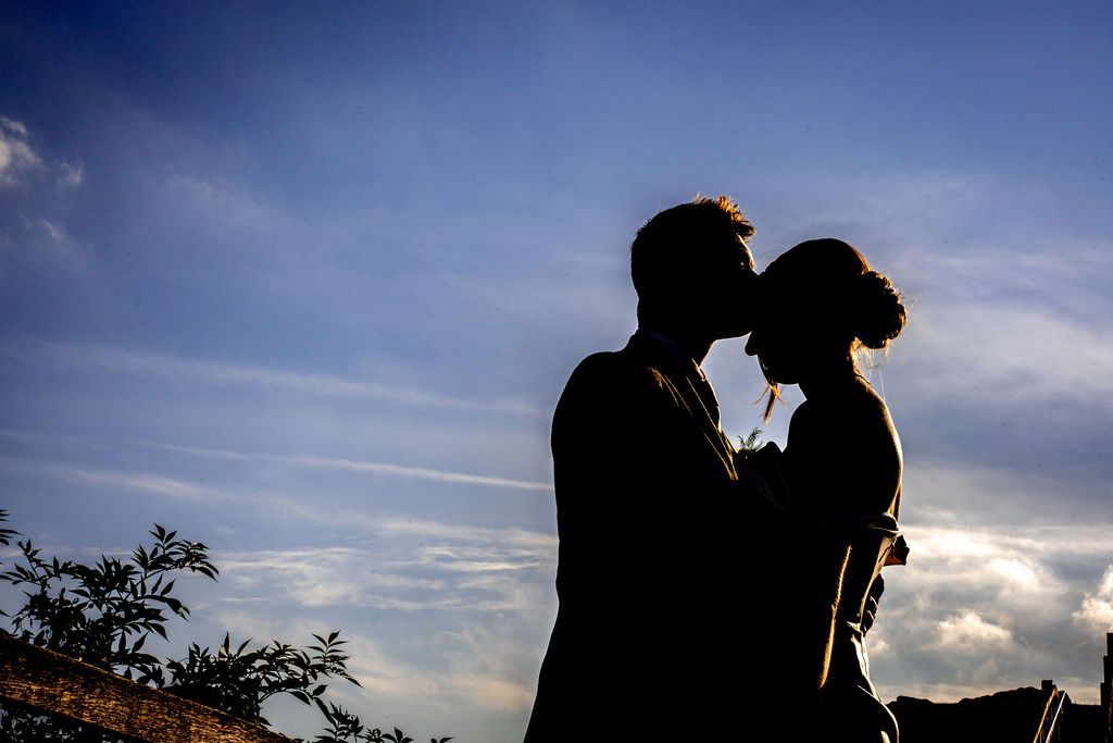 Silhouette of a romantic couple about to kiss against a dramatic blue sky at sunset.
