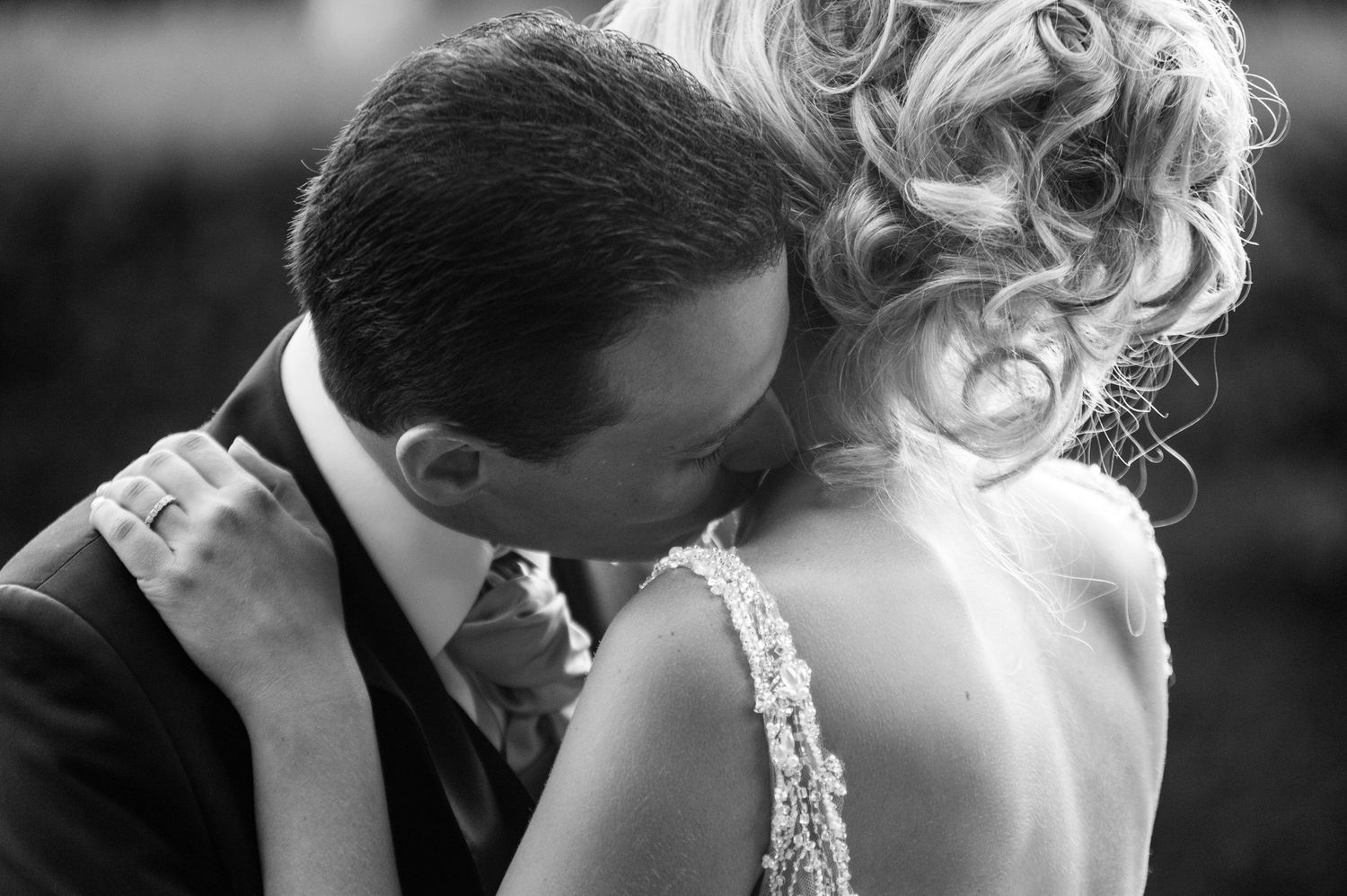 Black and white wedding photo of bride and groom sharing an intimate embrace, showcasing elegant bridal gown details.