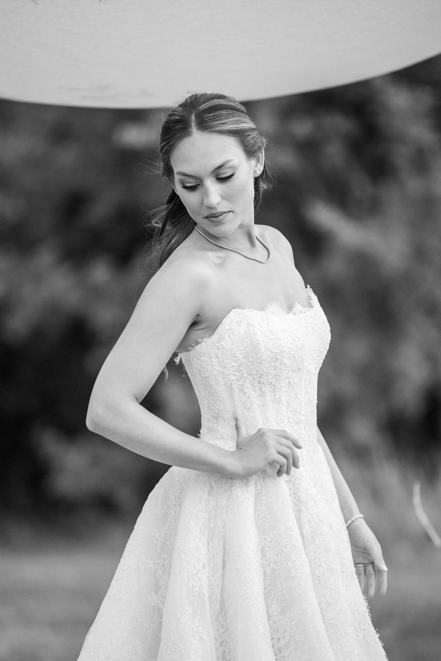 Black and white bridal portrait of a young woman in a strapless lace wedding gown posing outdoors.
