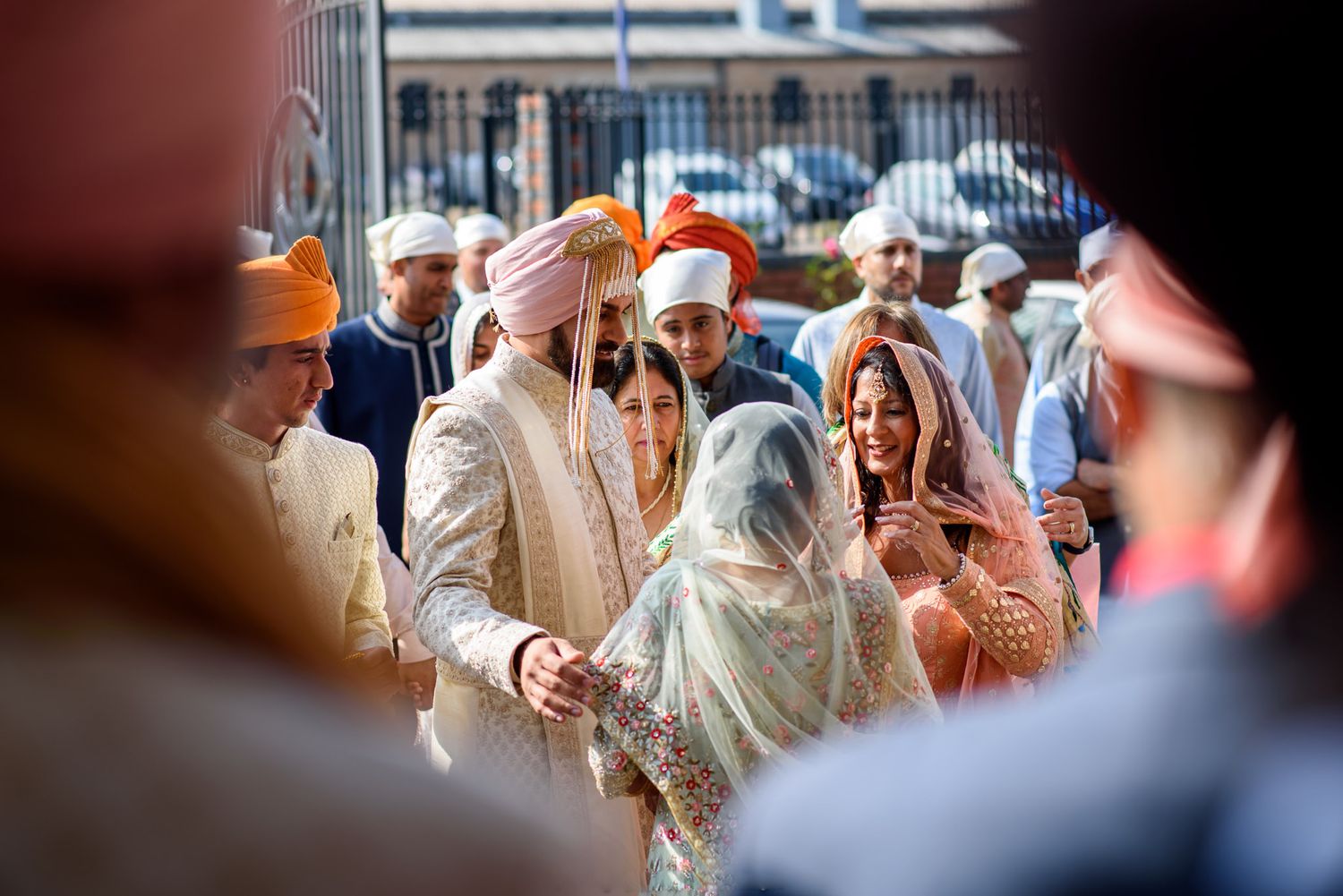 Sikh wedding ceremony with groom in golden sherwani and orange turban surrounded by guests in traditional attire.