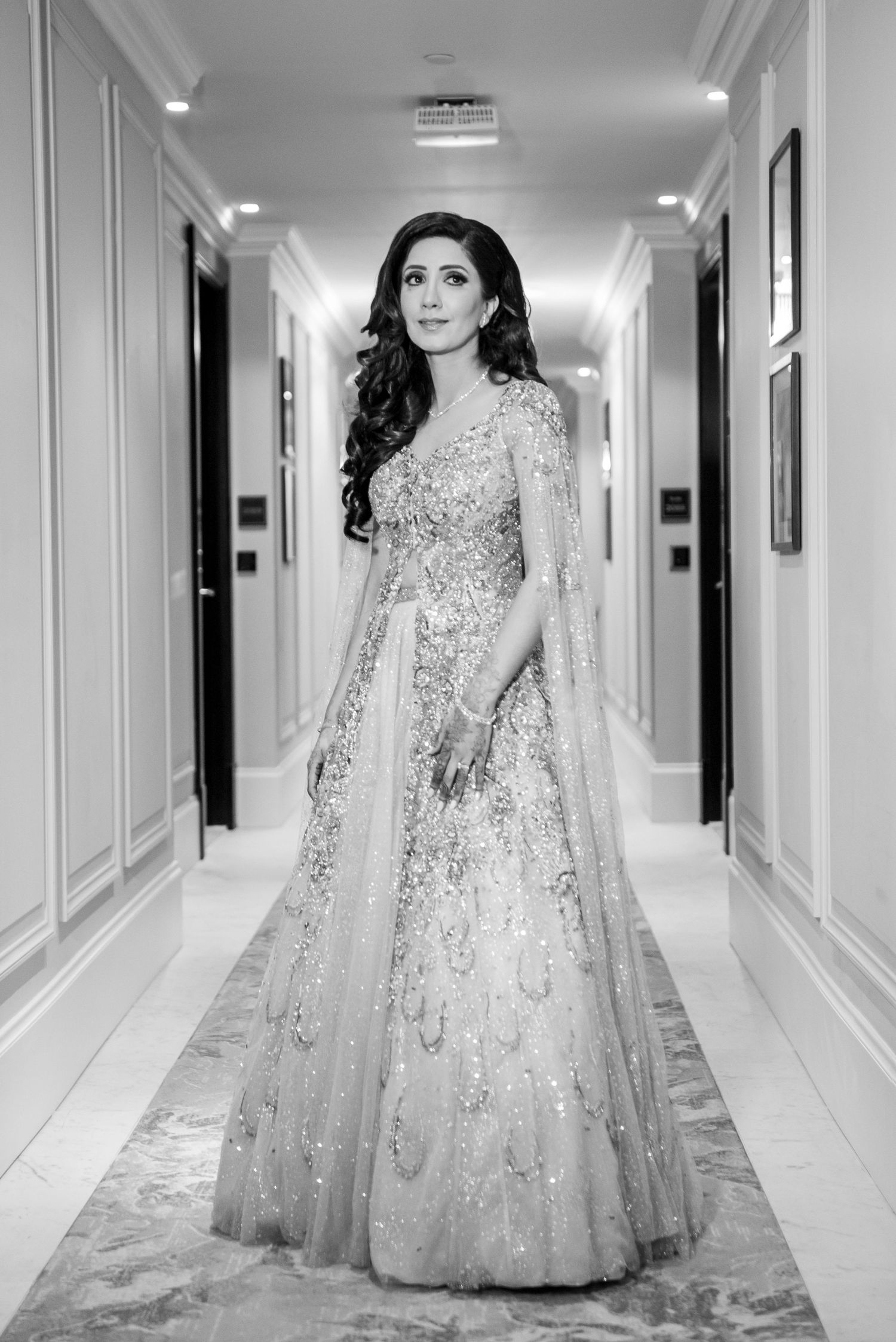 A bride in an elegant white embellished gown with long train poses in a luxurious hotel hallway.