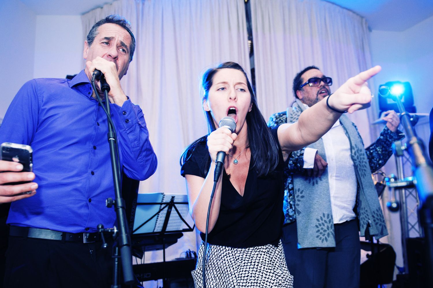 Band members in blue shirts perform energetically at an indoor event with blue lighting effects.