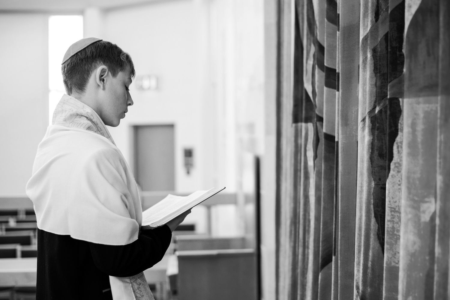 Professional in formal attire stands in a modern office hallway looking at paperwork.