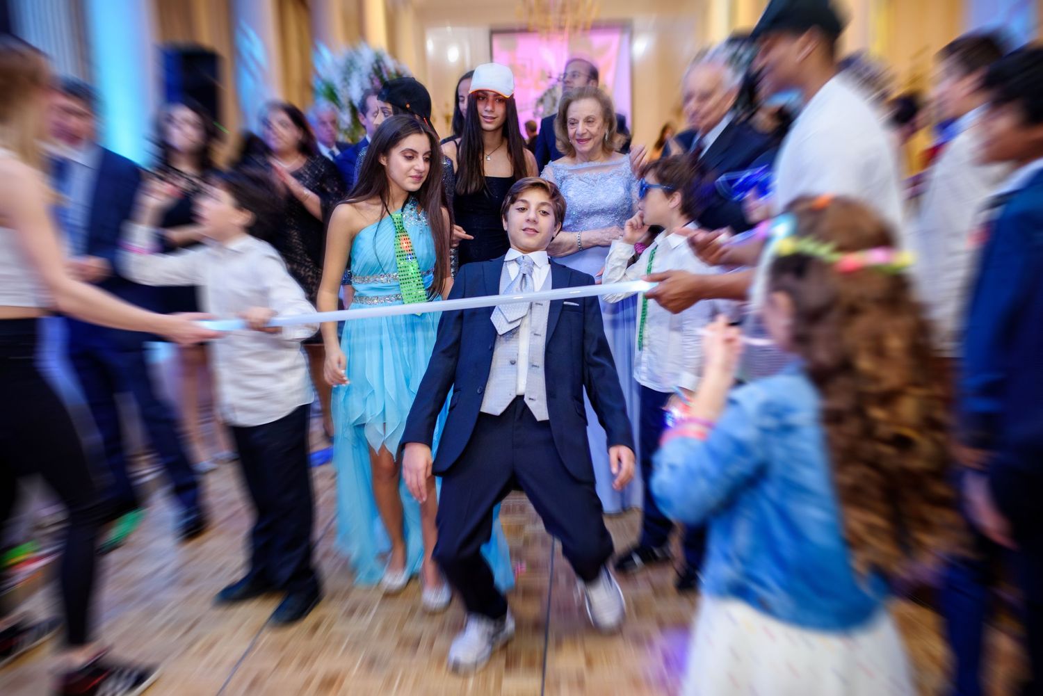 People dance and celebrate at a lively wedding reception with colorful lights and blurred motion.