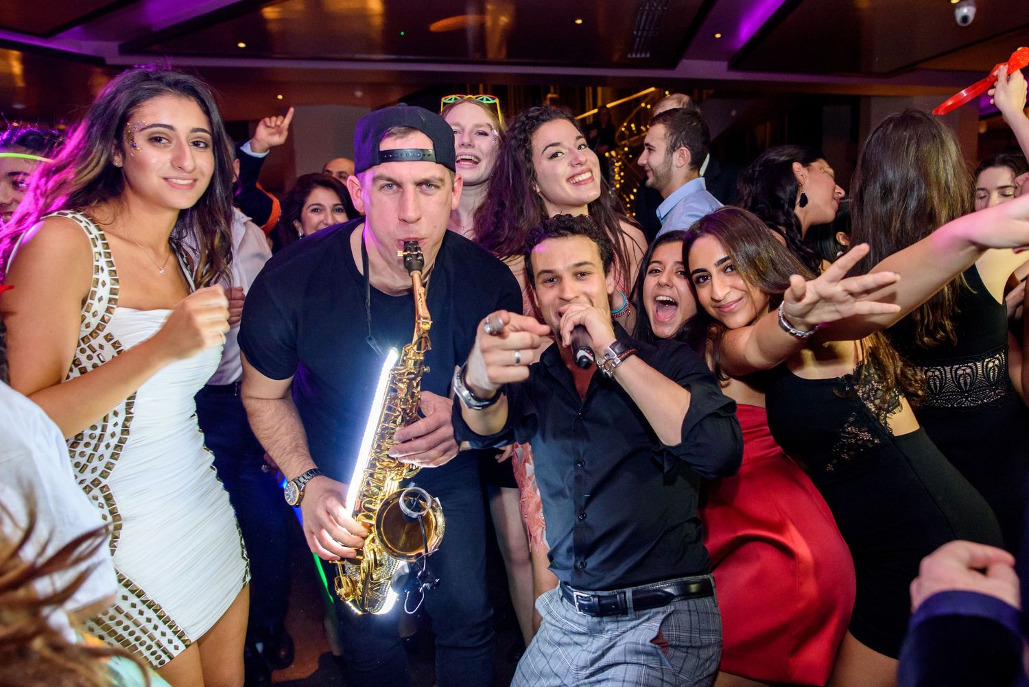 Lively dance party celebration with colorful purple lighting and a crowd on the dance floor.