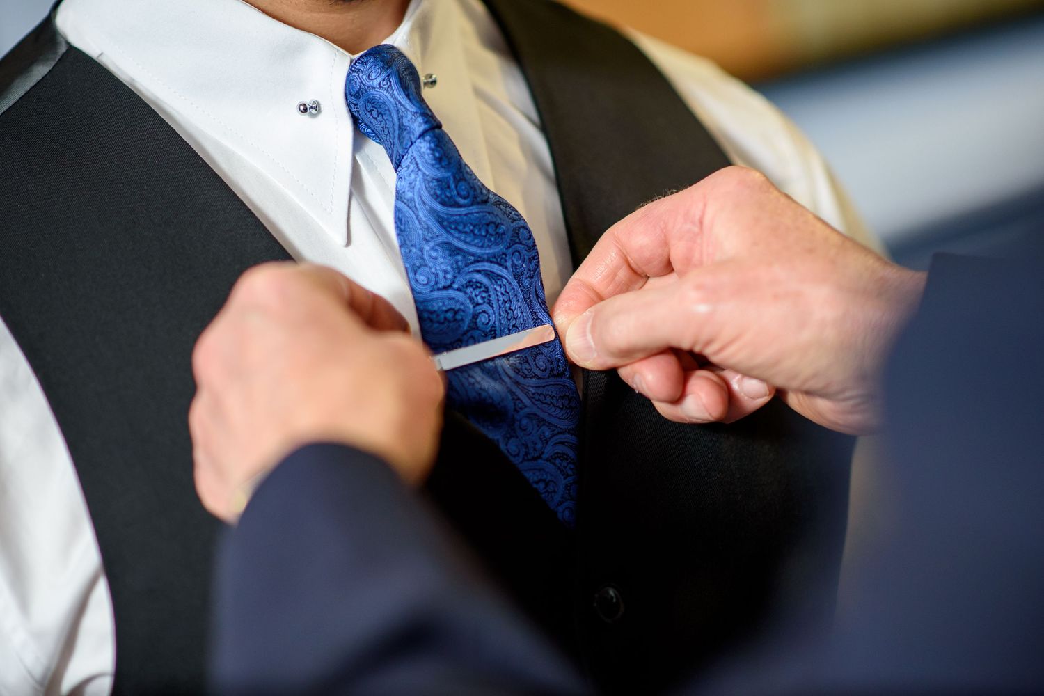 Professional in a dark suit adjusts their blue necktie while preparing for a formal event or meeting.