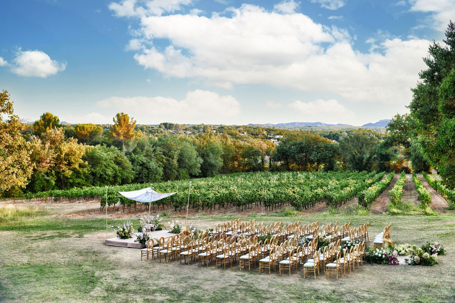 Panoramic view of an outdoor wedding ceremony setup with wooden chairs on a grassy lawn against a scenic mountain backdrop.