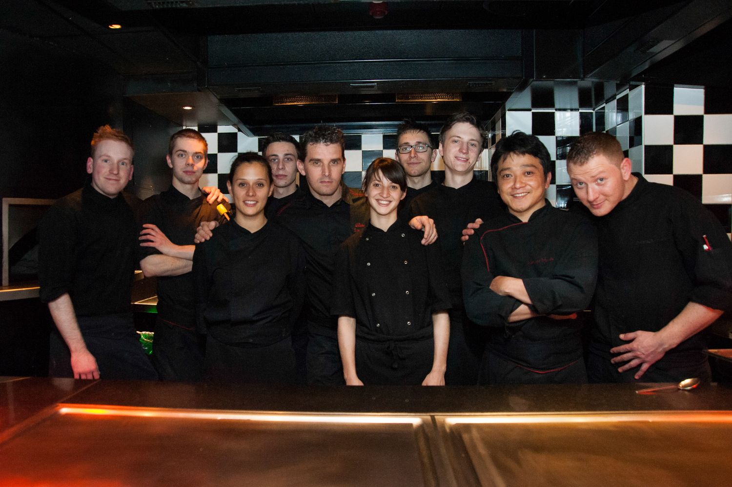 Group photo of staff members in black attire against a dark background.