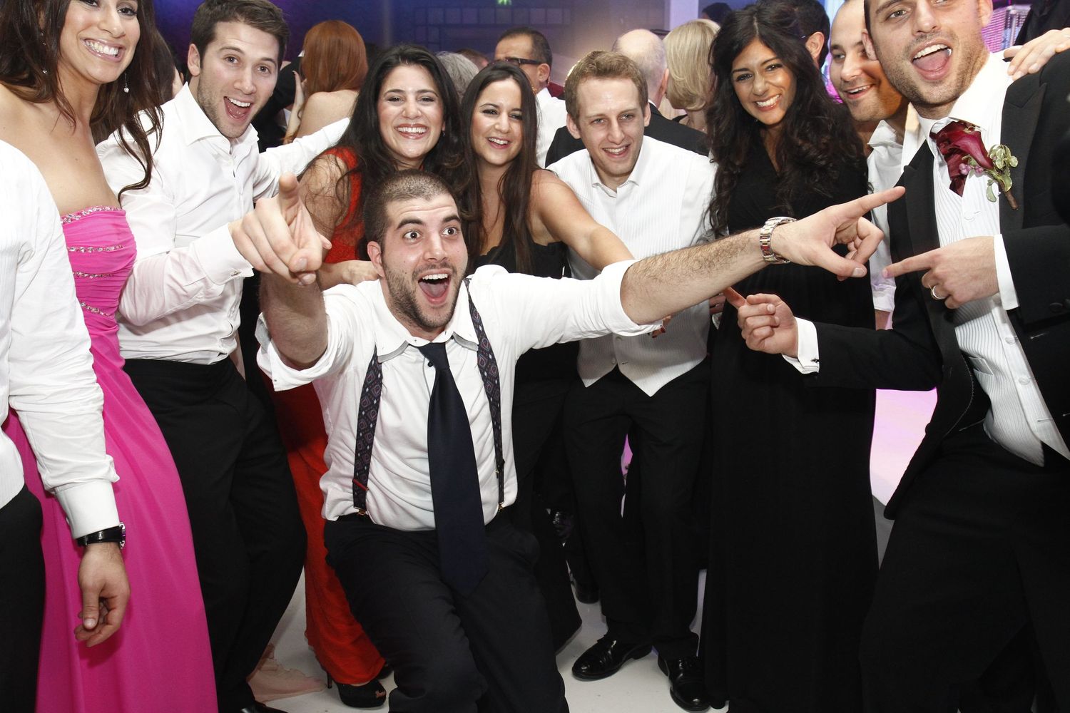A large group of formally dressed people pose together at a celebratory event with excited expressions.