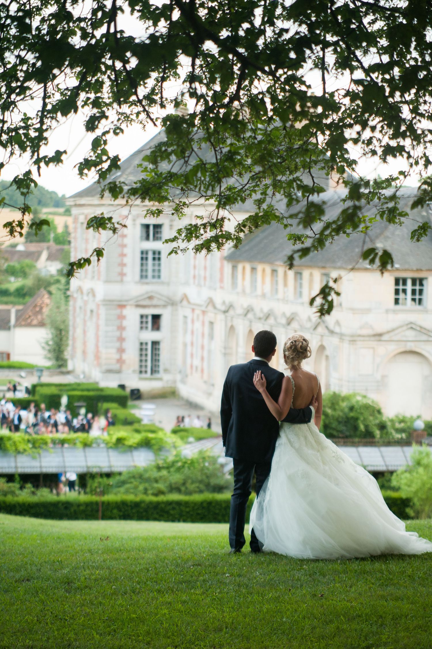 Bride and groom walk hand in hand toward a elegant French chateau venue surrounded by lush gardens.