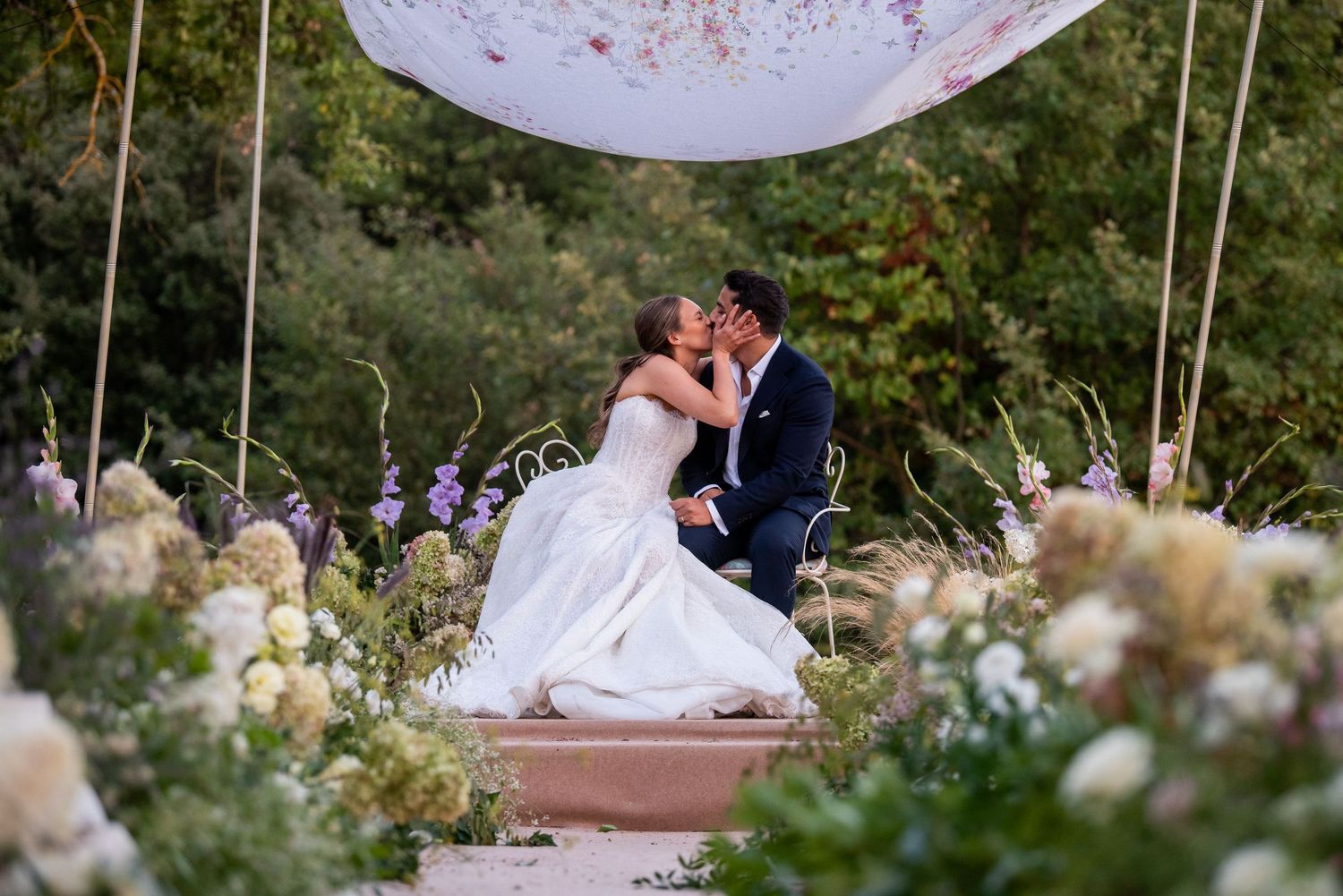 A couple in wedding attire shares an intimate moment in a lush garden setting during their special day.