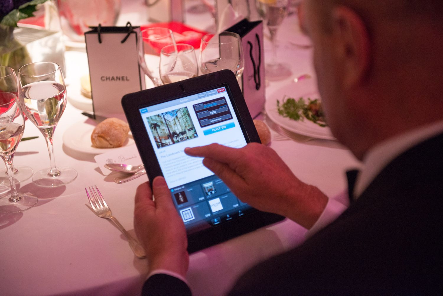 Guest using tablet device at formal dinner table with wine glasses.